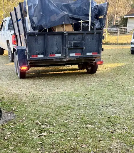 A loaded stake-bed trailer, tarped and parked on a lawn after a Junk Doctor pickup