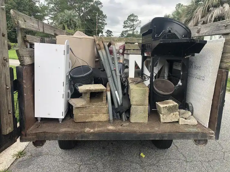 A loaded flatbed trailer stacked with cabinets, a grill, pipe and buckets